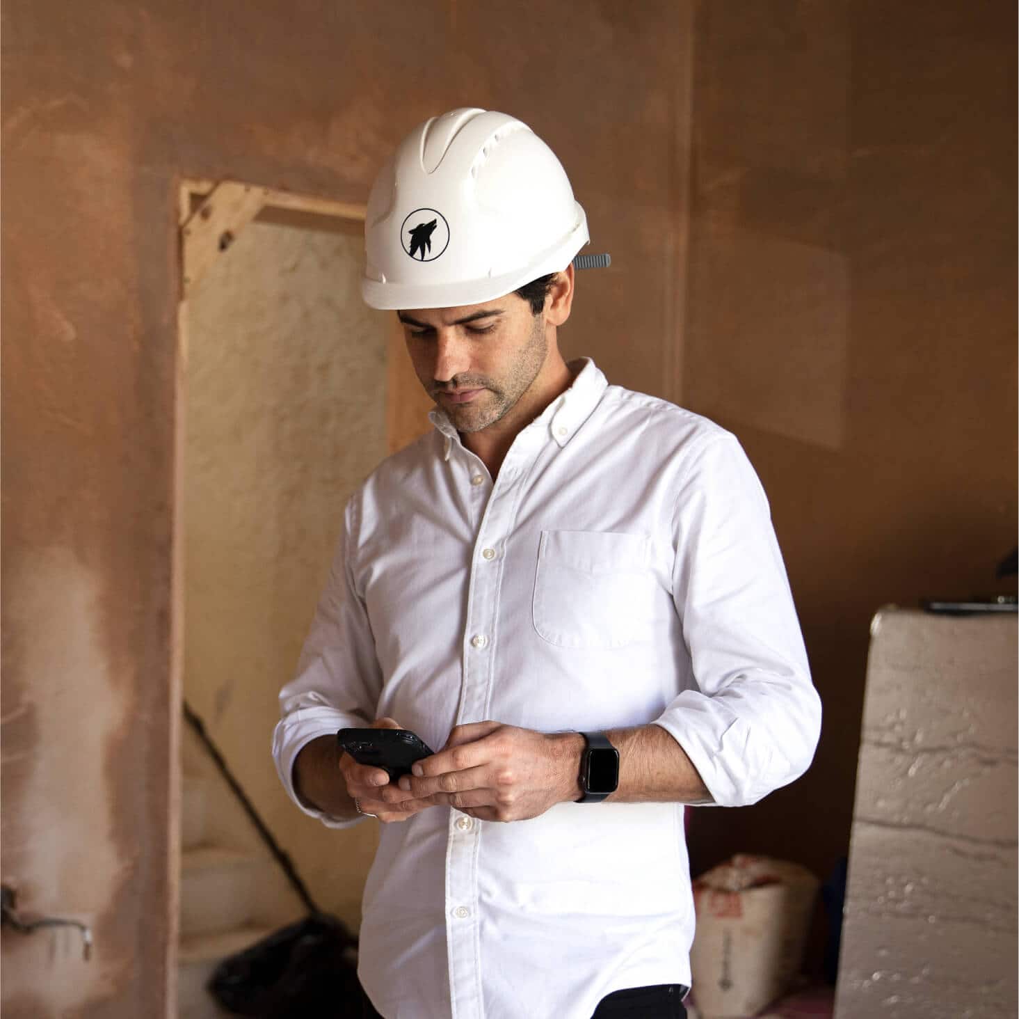 A carpenter on a building site enters the costs of materials into job management software on their mobile device.